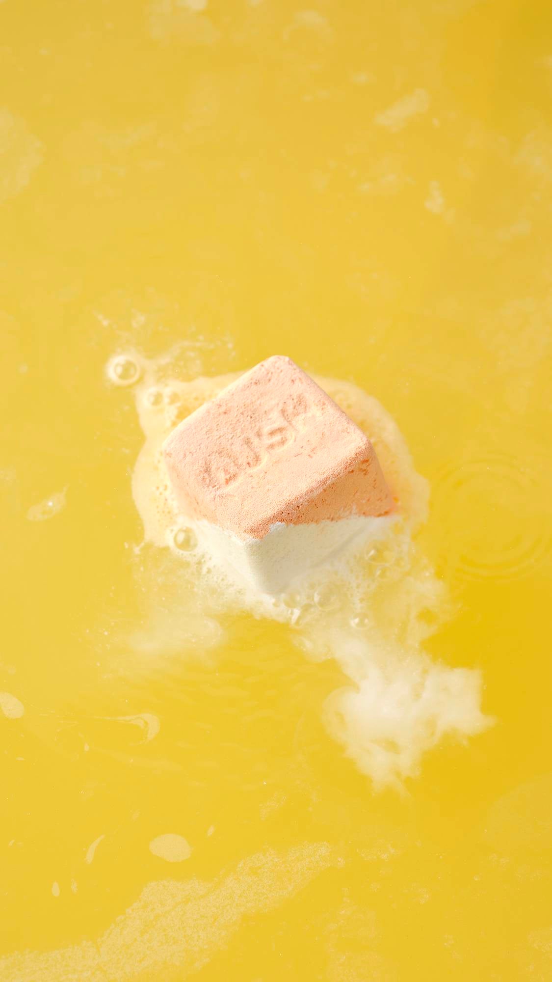 The Cold Water Soother bath bomb dissolves on the surface, releasing white, frothy foam and vibrant swirls that ripple across the water.