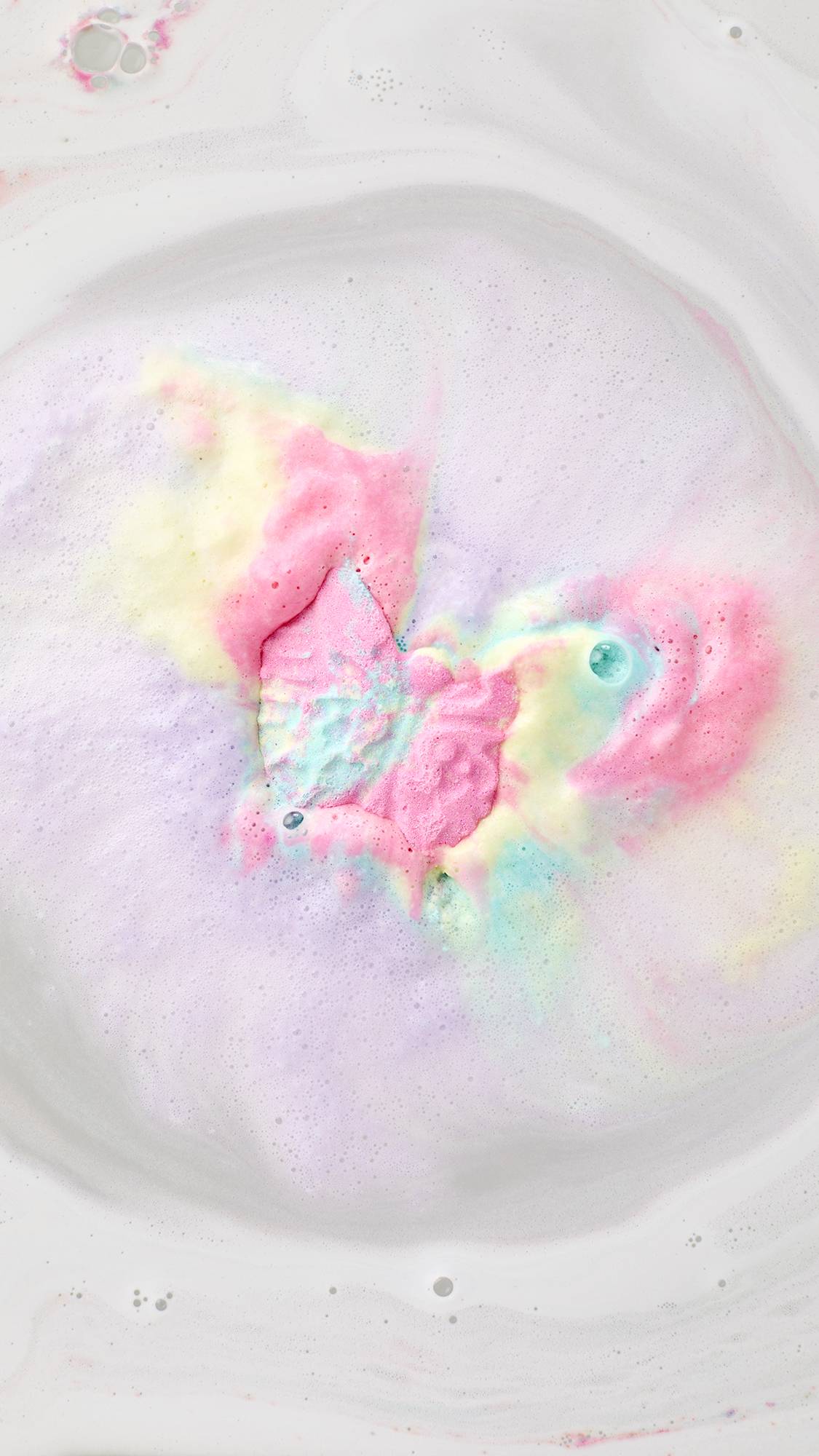 A top-down view of the Luna Butterfly bath bomb dissolving in milky white water. It creates a vibrant "bath art" explosion of neon pink, soft yellow, and bright turquoise foam that swirls outward in a cloud of colorful bubbles.