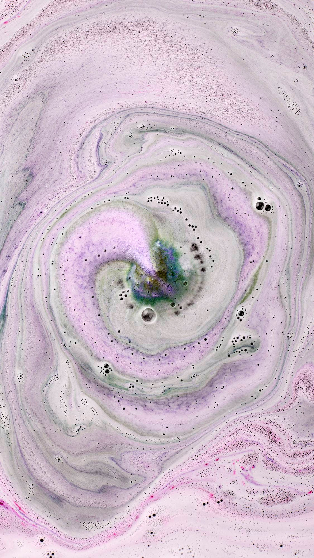 Black Rose. An aerial view shows the dark rose-shaped bath bomb as it has nearly fully dissolved. The water is a deep, velvety purple and pink, covered in a thick layer of shimmering silver plastic-free glitter and delicate bubbles.