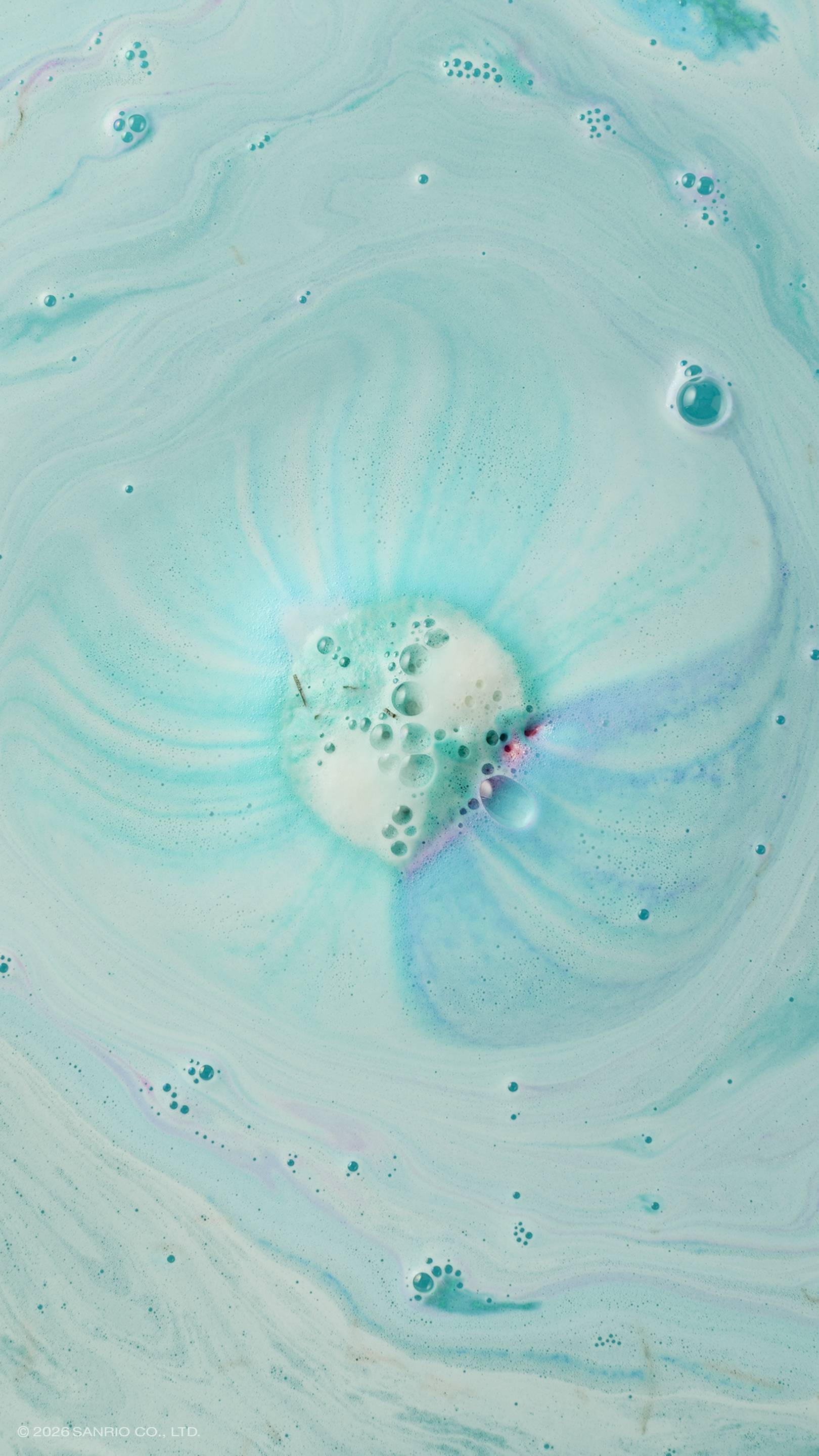 An aerial shot of turquoise bath water swirling with white foam and bubbles. In the centre, a bath bomb has mostly dissolved, leaving behind a circular patch of froth with faint streaks of purple and dark teal radiating outwards.