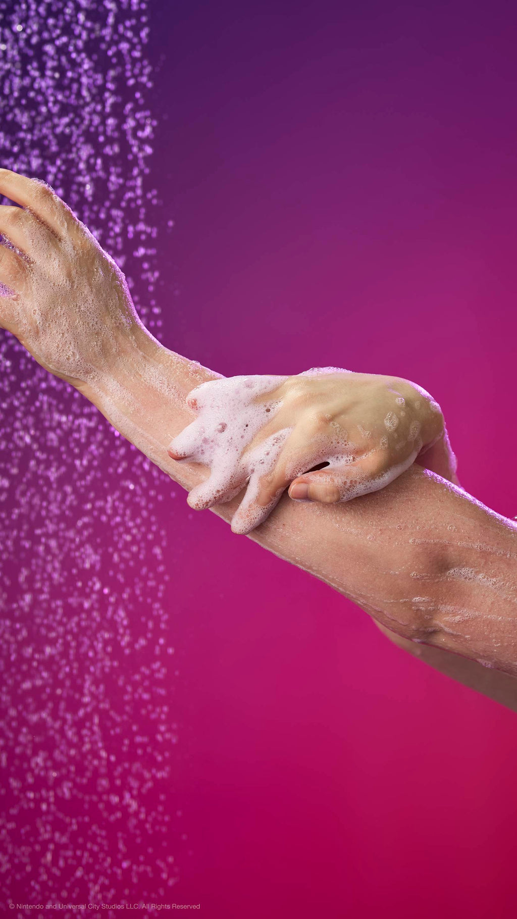 Hands lather white foam onto an arm under a shower spray against a purple and pink gradient background.