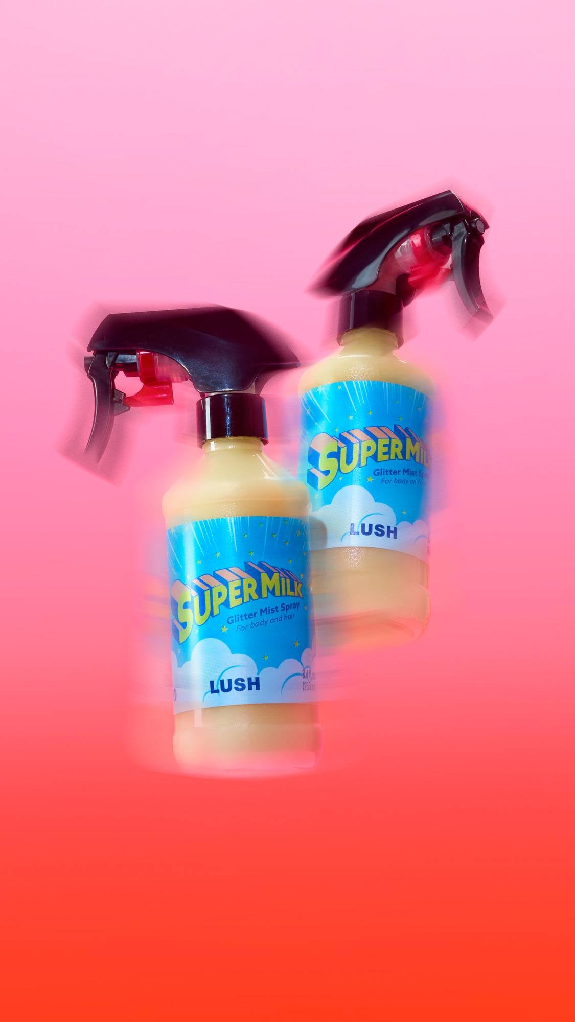 Two bottles of Lush 'Super Milk' Glitter Mist Spray appear to float with a dynamic motion-blur effect against a vibrant pink-to-red gradient background. The cream-coloured liquid and bright blue labels stand out in the energetic composition.