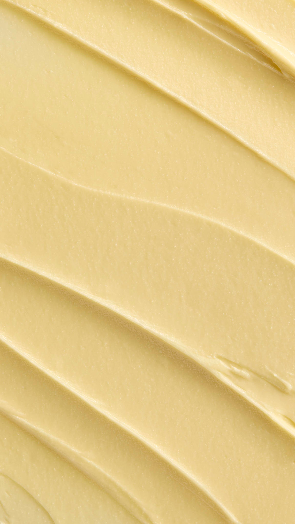 A super close-up image showing diagonal, overlapping smears of the thick, creamy, pale yellow Lush "Acai & Sacha Inchi" Vitamin E facial cleanser. The smooth product has a matte finish and subtle ridged textures.