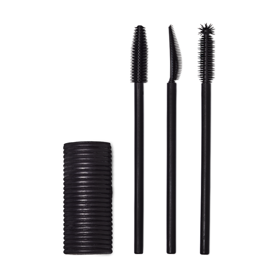 A Solid cylindrical block of black mascara next to three different style mascara spoolie brushes.