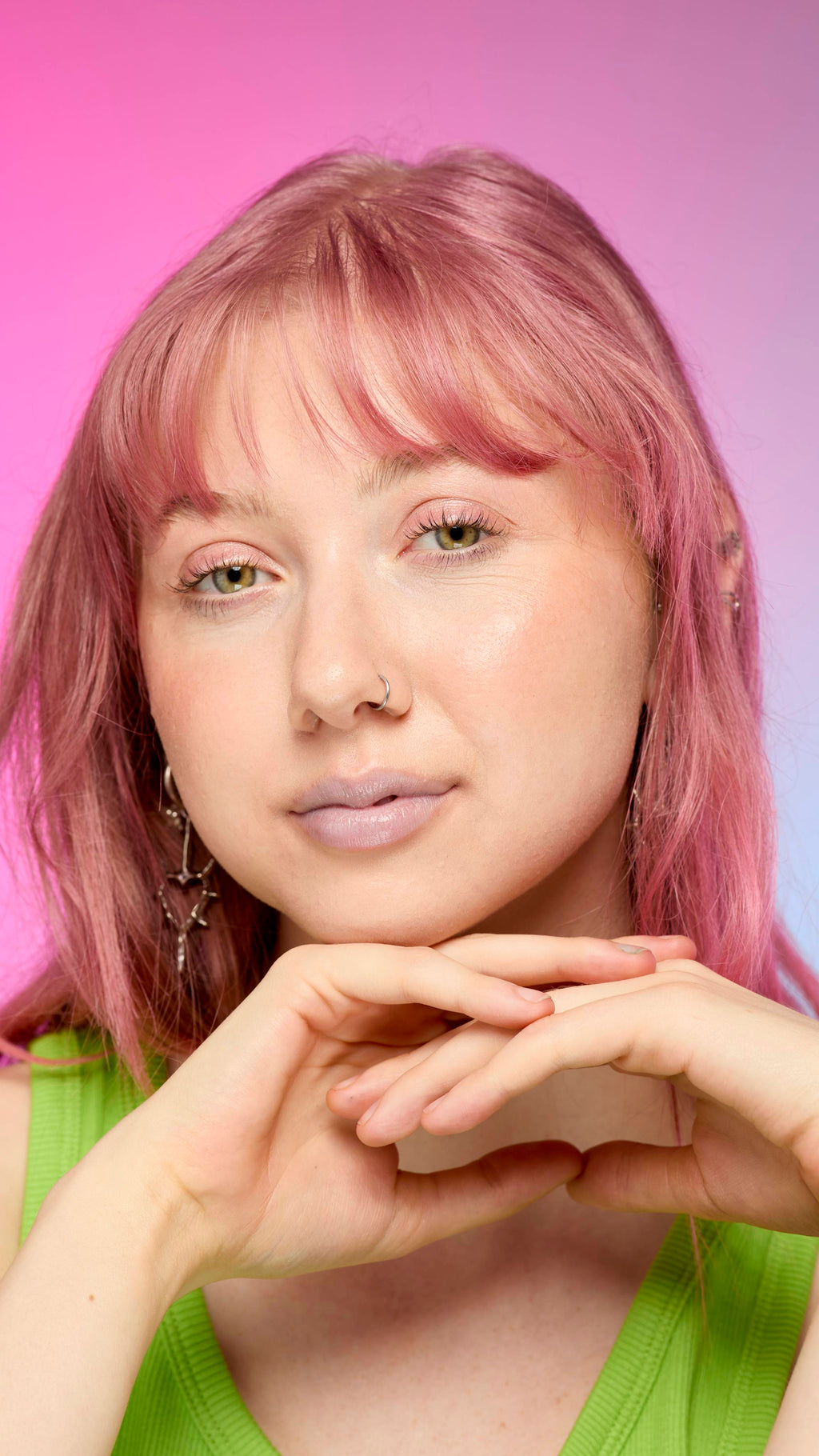 The image shows a fair-skinned model on a pink and blue gradient background. They have pink hair and subtle, blue shimmering lips from using the Blue Pearl lip cream.