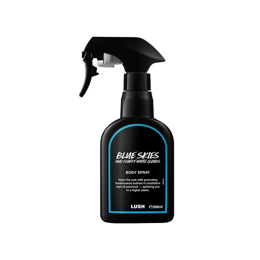 A recycled black plastic LUSH body spray bottle with a trigger nozzle stands upright with a blue rimmed label with white text that reads "Blue Skies and Fluffy White Clouds Body Spray".