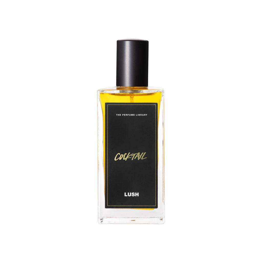 A glass perfume bottle filled with light amber liquid. A black label reads 'The Perfume Library' and 'Cocktail'.