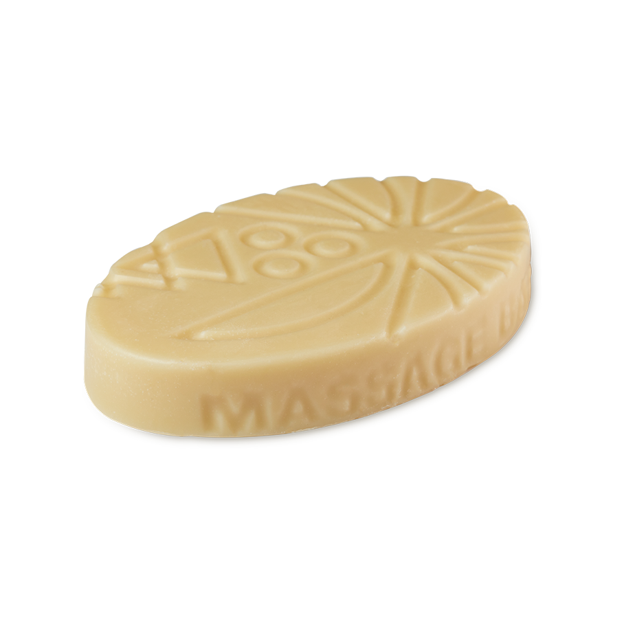 Coconut Drench. An oval, cream-coloured solid Lush massage bar with geometric and sunburst patterns embossed on top. The words 'MASSAGE BAR' are embossed along the curved side.