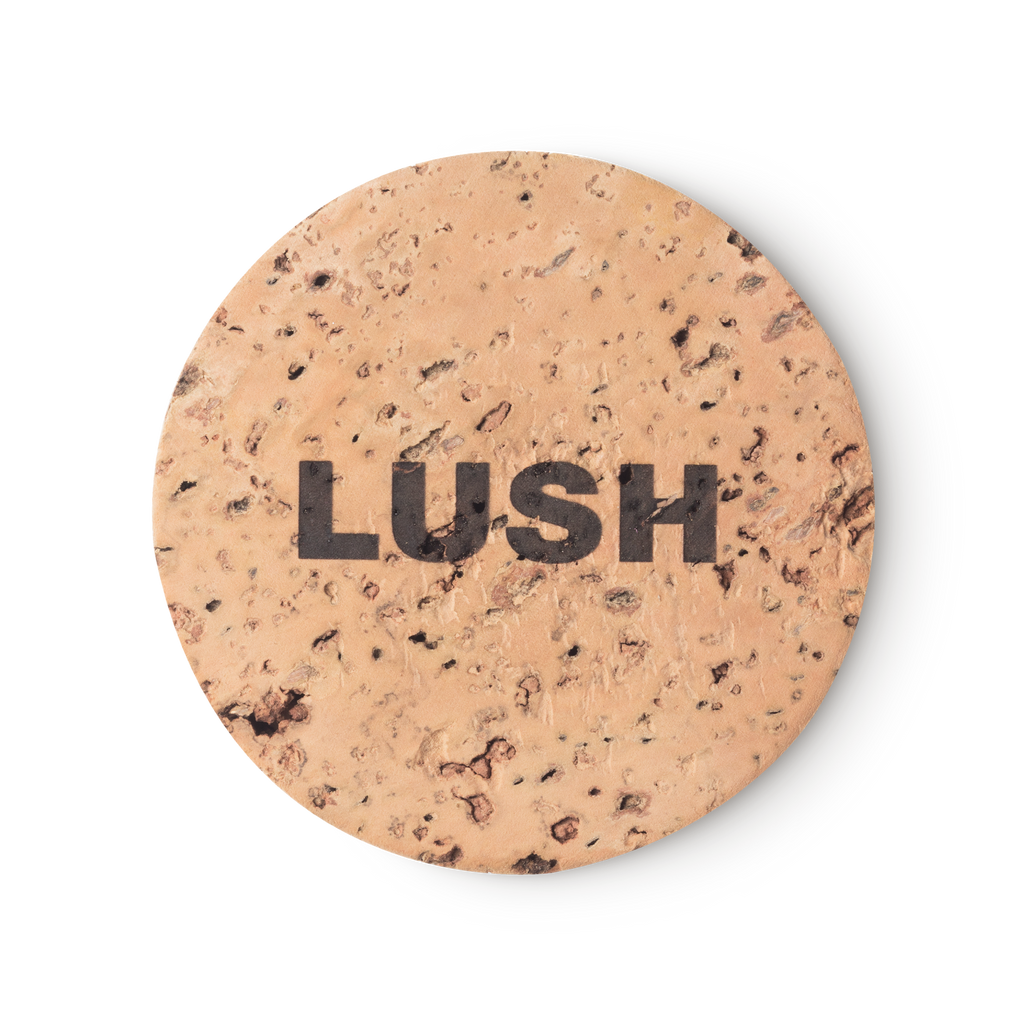 Cork Pot. A round, beige, product holder made of natural cork. LUSH is printed on top, in black, bold letters.
