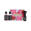 A LUSH Crush gift set featuring a brightly colored box with pink roses, next to three small black and white bottles: "Rascal" exfoliating shower gel, "Rebel" body lotion, and "Brat" body spray.