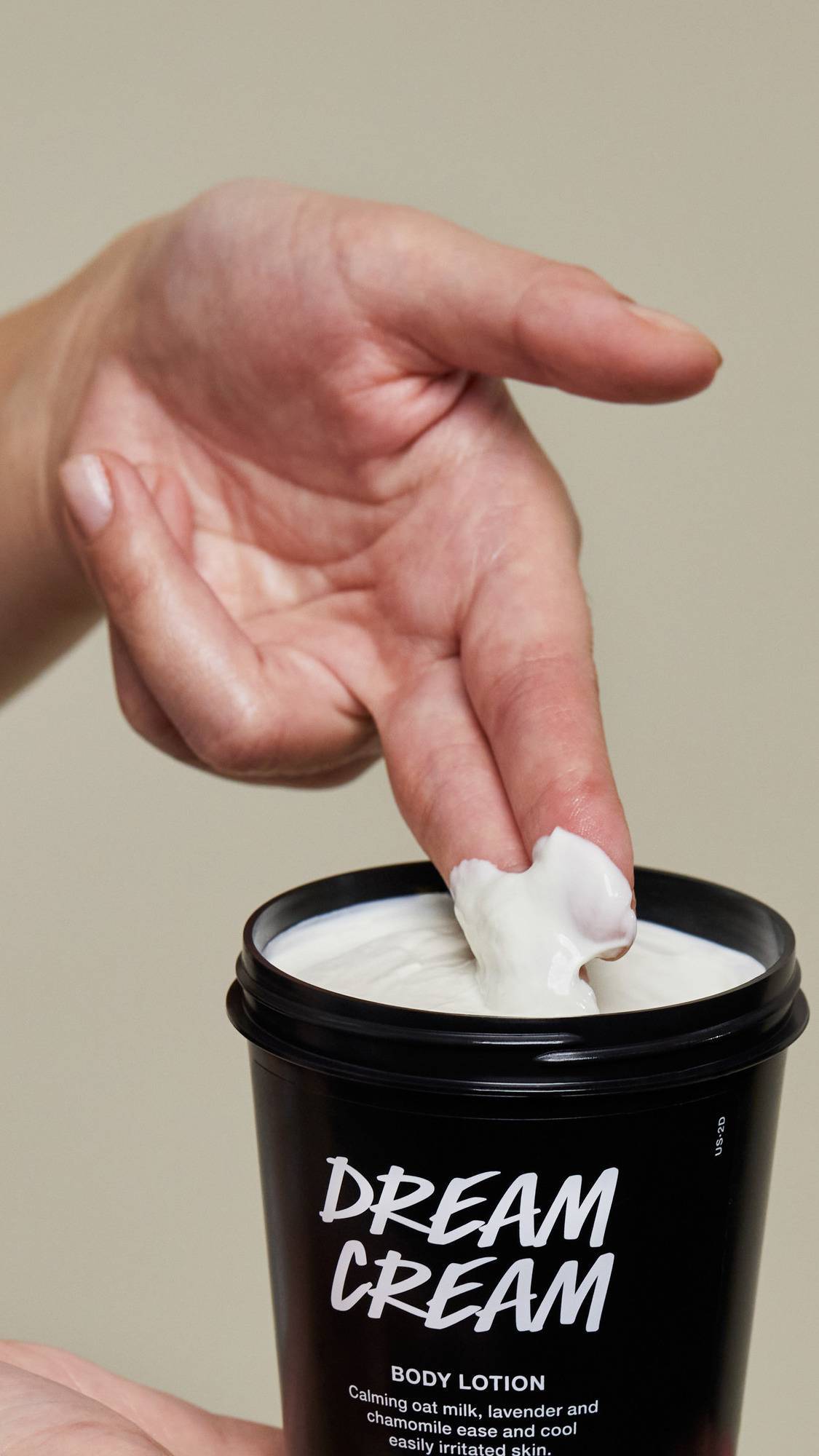 The image shows a close-up shot of the black, recycled plastic pot as the model scoops out the Dream Cream product with two fingers.