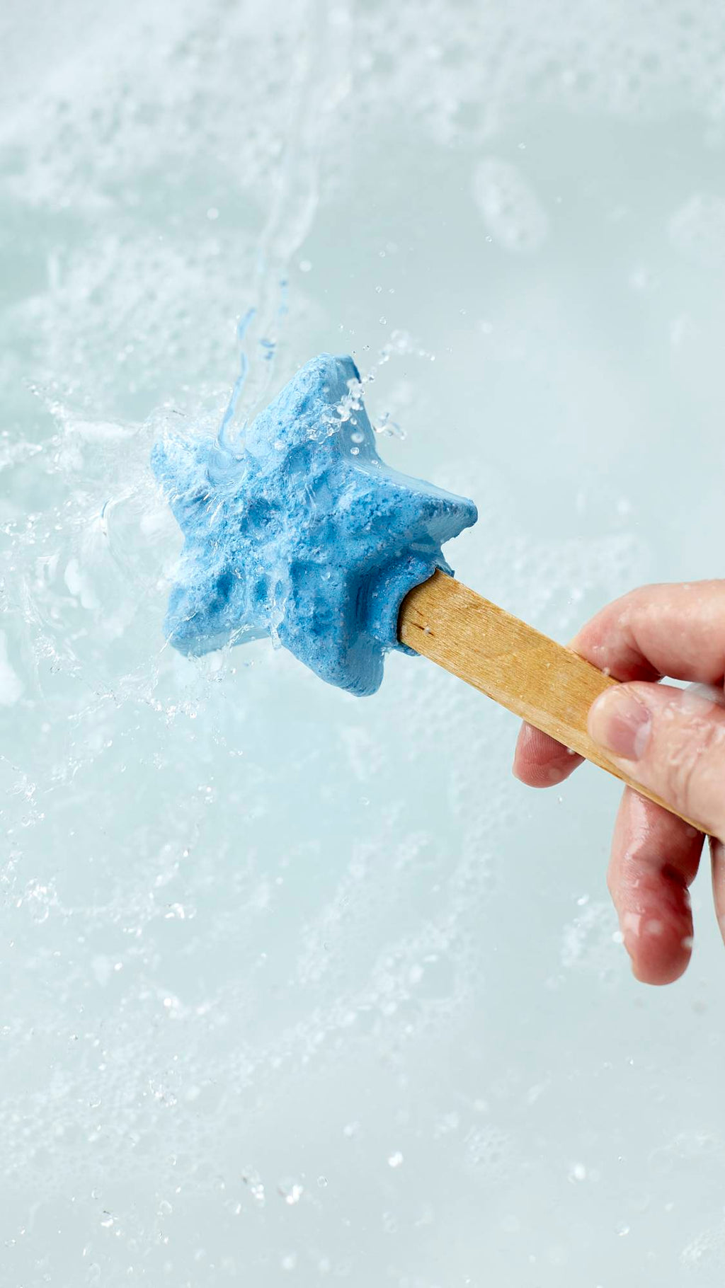 The image shows a close-up shot of the Frozen reusable bubble bar stick being held under running tap water. The icy-blue star at the end creates bubbly, cool-blue water below.
