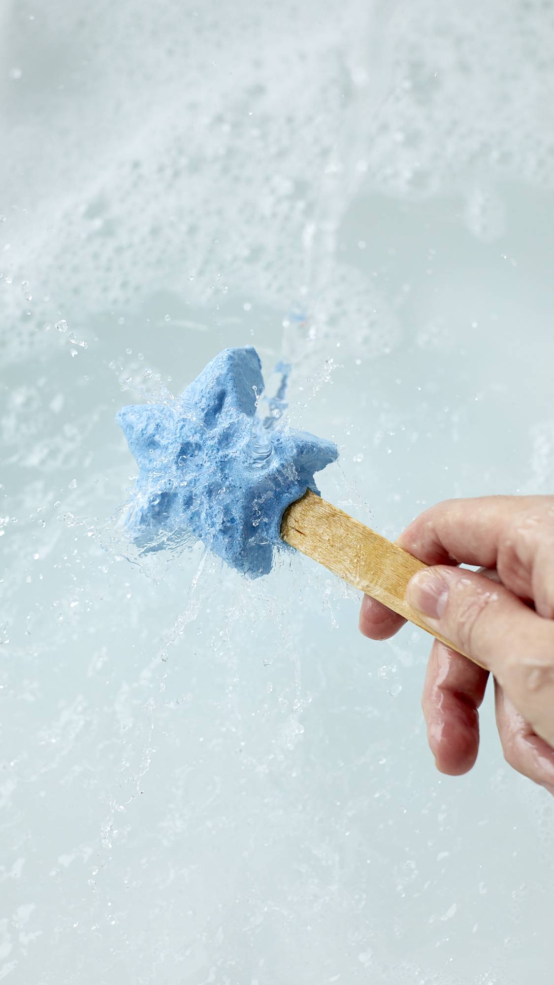 The image shows a close-up shot of the Frozen reusable bubble bar stick being held under running tap water. The icy-blue star at the end creates bubbly, cool-blue water below.
