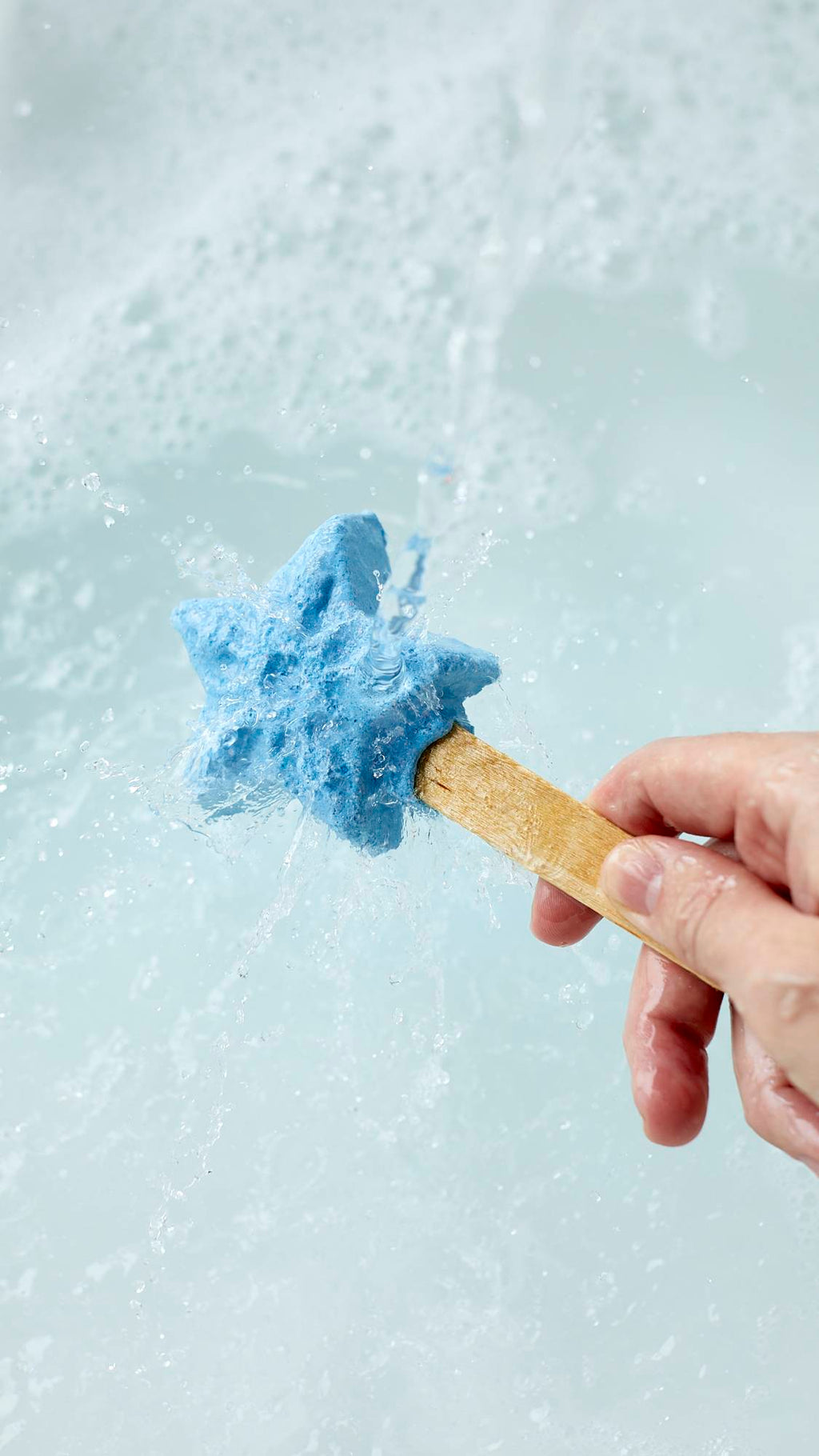 The image shows a close-up shot of the Frozen reusable bubble bar stick being held under running tap water. The icy-blue star at the end creates bubbly, cool-blue water below.