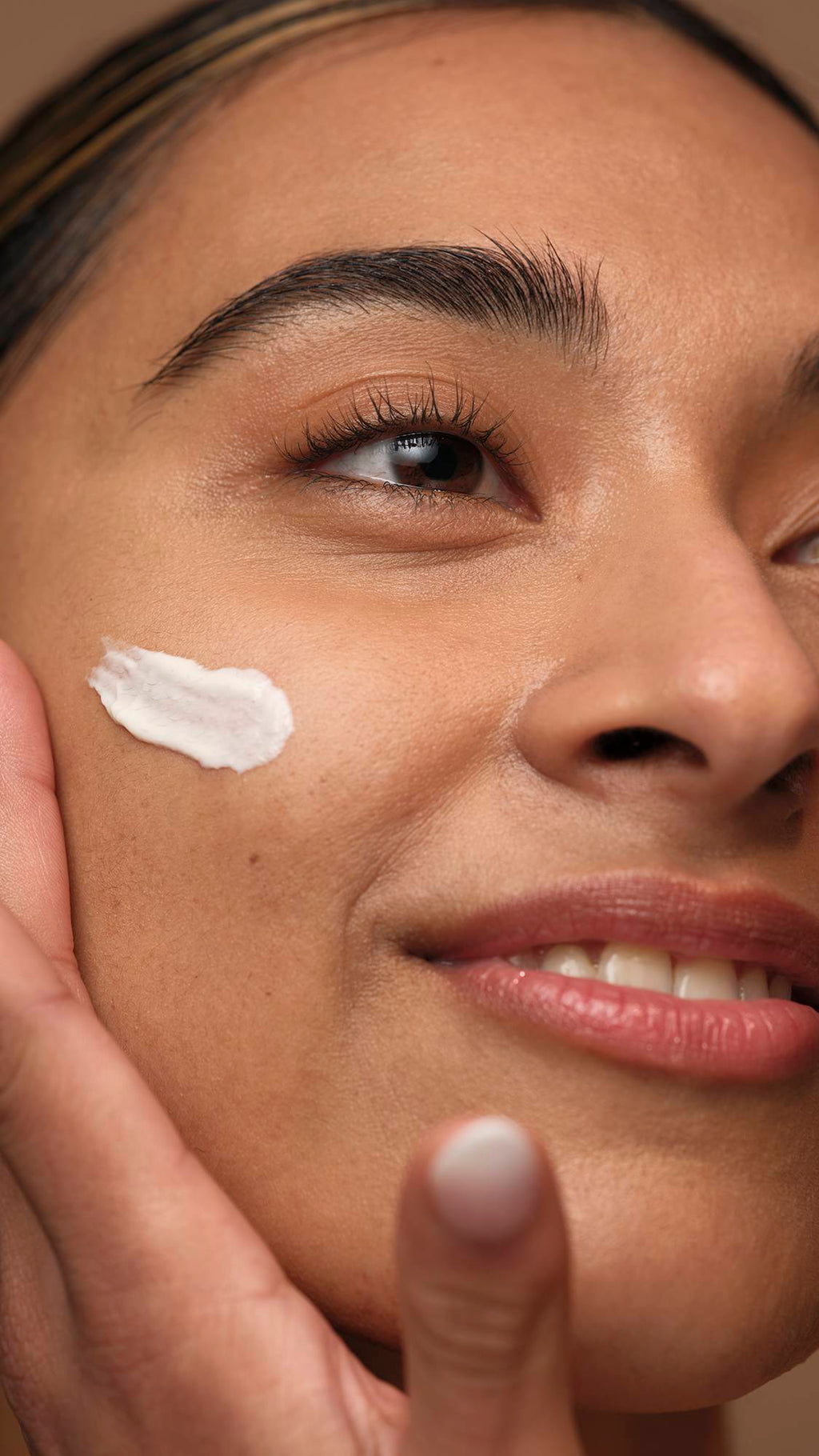 A super close-up of the model's side of their face smiling widely as they smooth the Gorgeous self-preserving moisturiser over their cheek.