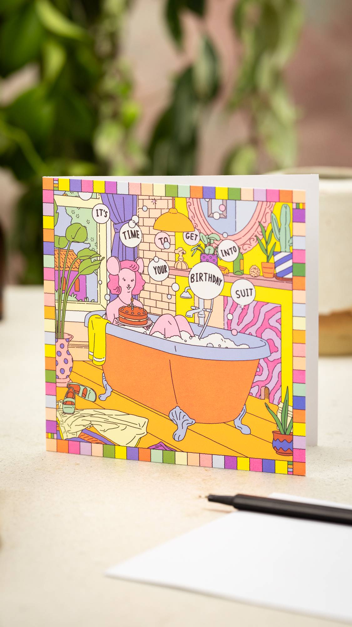 Image shows the It's Time To Get Into Your Birthday Suit card stood on a table with an envelope and pen in front.