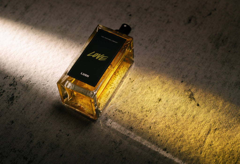 Love, a bottled, black label perfume, lies flat, with light shining through it, creating a golden cast of light.