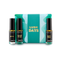 The image shows a "LUSH DAYS" perfume gift set. Three cylindrical glass perfume bottles are arranged around a vibrant teal box with a wavy pattern and yellow text. Perfumes include 'Grass', 'Breath of God' and 'Dear John'.
