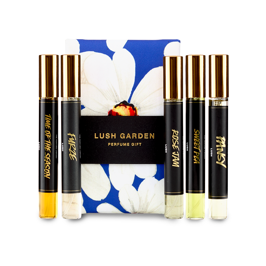 The image shows a "LUSH GARDEN" perfume gift set. Five thin, cylindrical glass perfume bottles with amber and clear liquids are arranged around a dark blue box featuring a large white floral design.