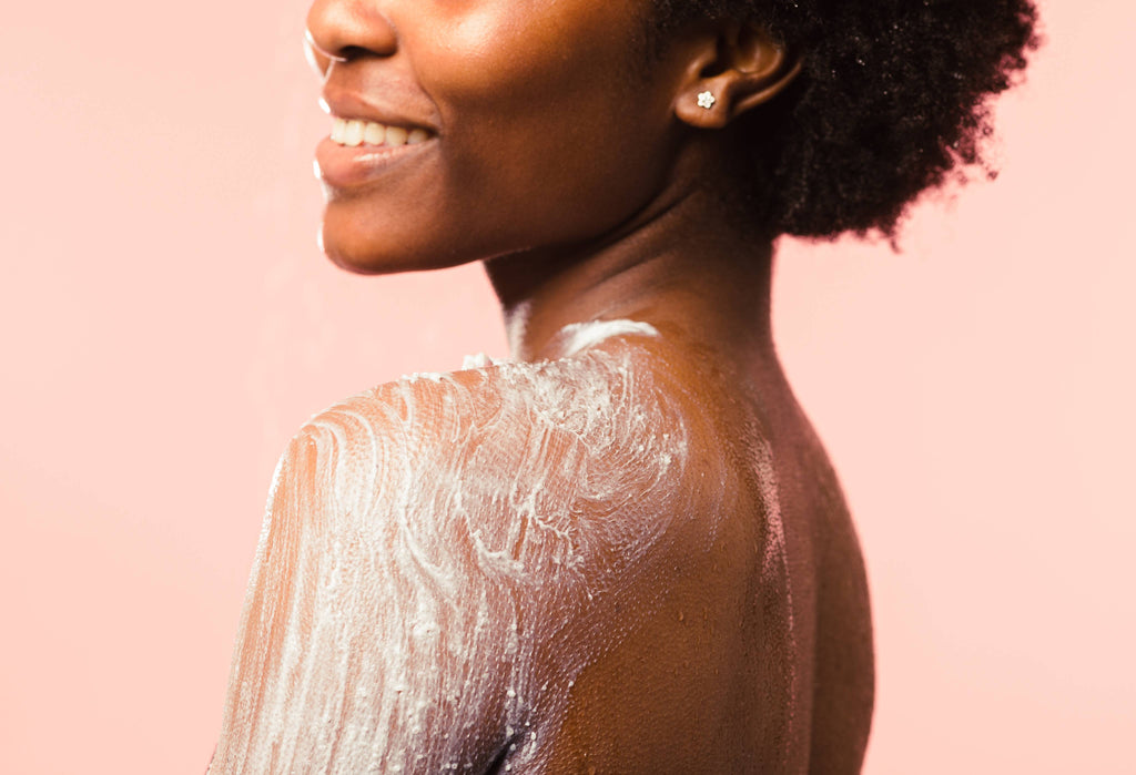 A cropped image of the model side-on from their cheeks to their upper arm as they stand on a pastel salmon background. They have rubbed the Ocean Salt scrub over their shoulder.