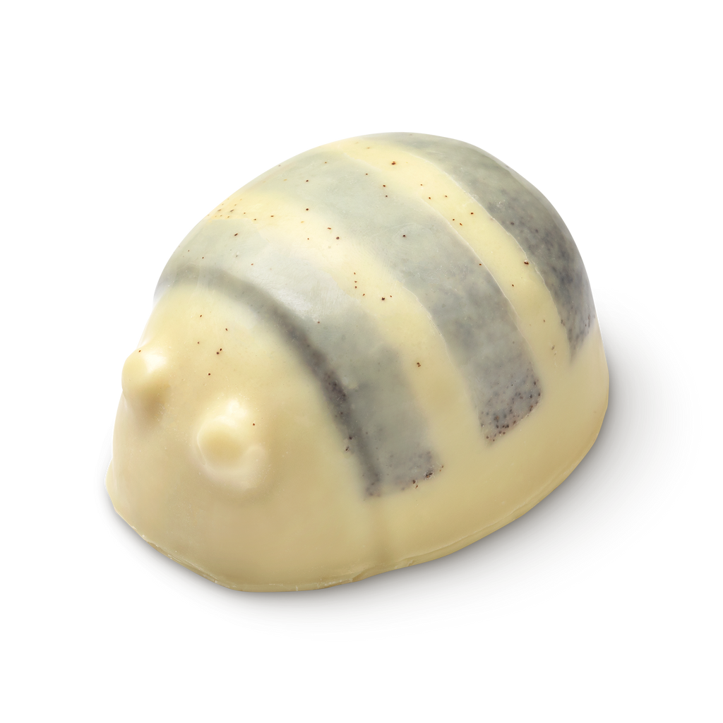 Scrubee solid body butter. The image shows a pale cream, bee-shaped product with a rounded top and small eyes. It features three, textured stripes across its back, appearing smooth and solid.
