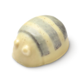 Scrubee solid body butter. The image shows a pale cream, bee-shaped product with a rounded top and small eyes. It features three, textured stripes across its back, appearing smooth and solid.