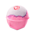 The Sex Bomb Bath Bomb features a vibrant pink lower half and a soft, pale purple top, separated by a thin, darker purple line. A delicate pink rosebud is nestled into the very top of the sphere, adding a romantic touch.