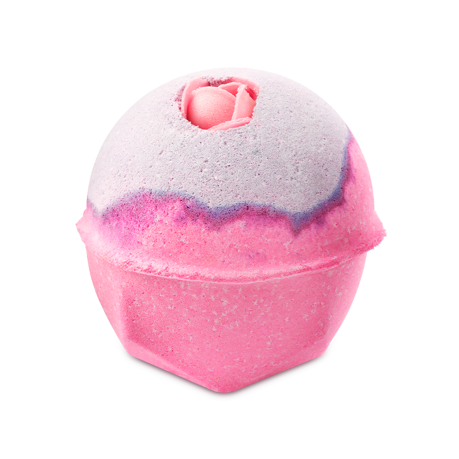 The Sex Bomb Bath Bomb features a vibrant pink lower half and a soft, pale purple top, separated by a thin, darker purple line. A delicate pink rosebud is nestled into the very top of the sphere, adding a romantic touch.