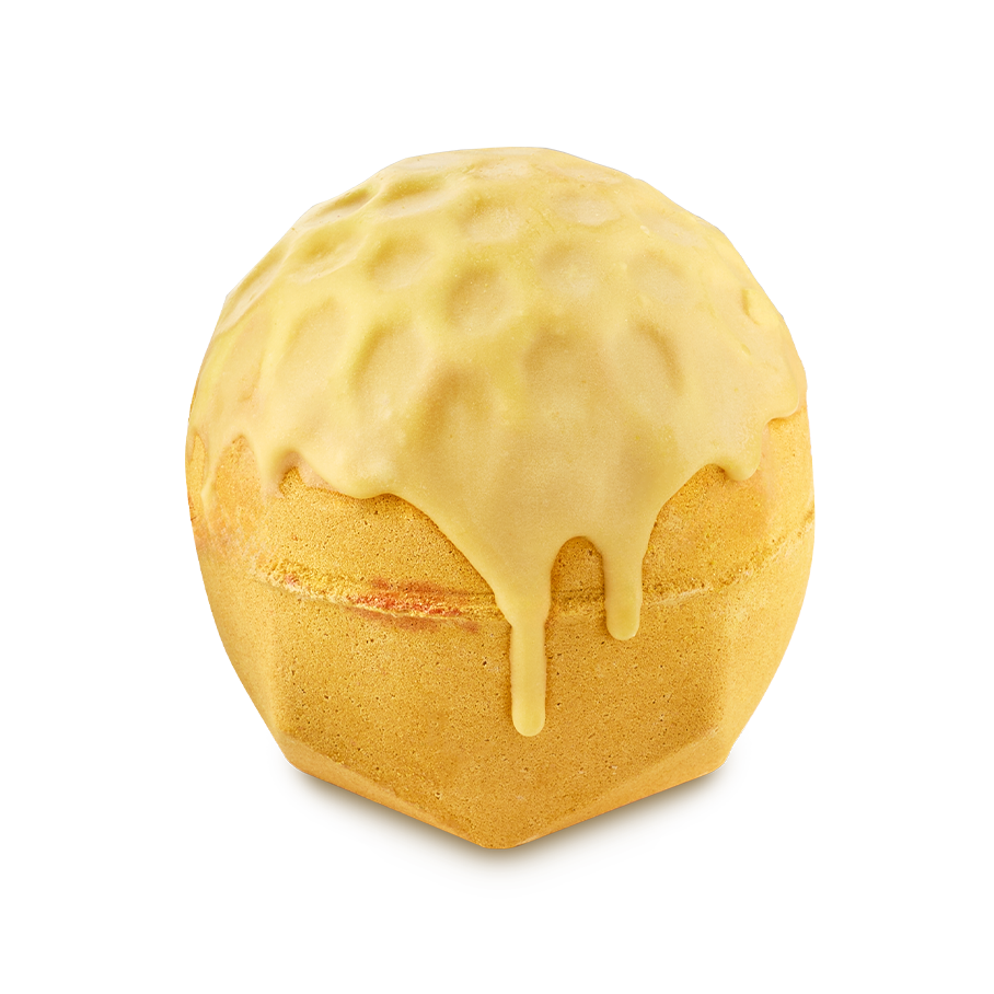 Sweet As Honey. A spherical, golden-yellow bath bomb with a faceted, flat base. It has a honeycomb-textured top that appears to be melting or dripping down the sides like thick honey.