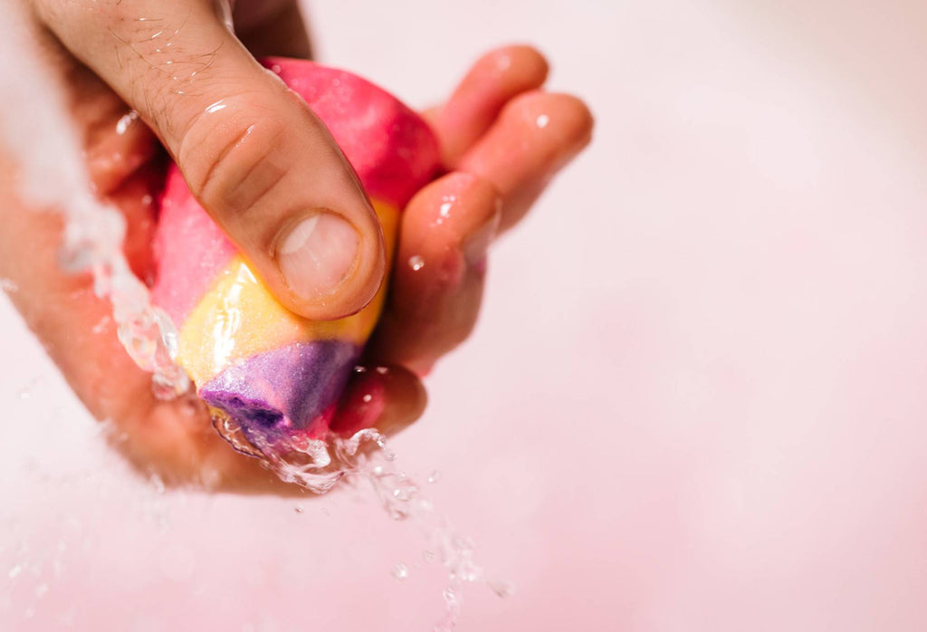 A snapped section of Unicorn Horn is held by a hand as water runs over it. The water in the background is light pink.
